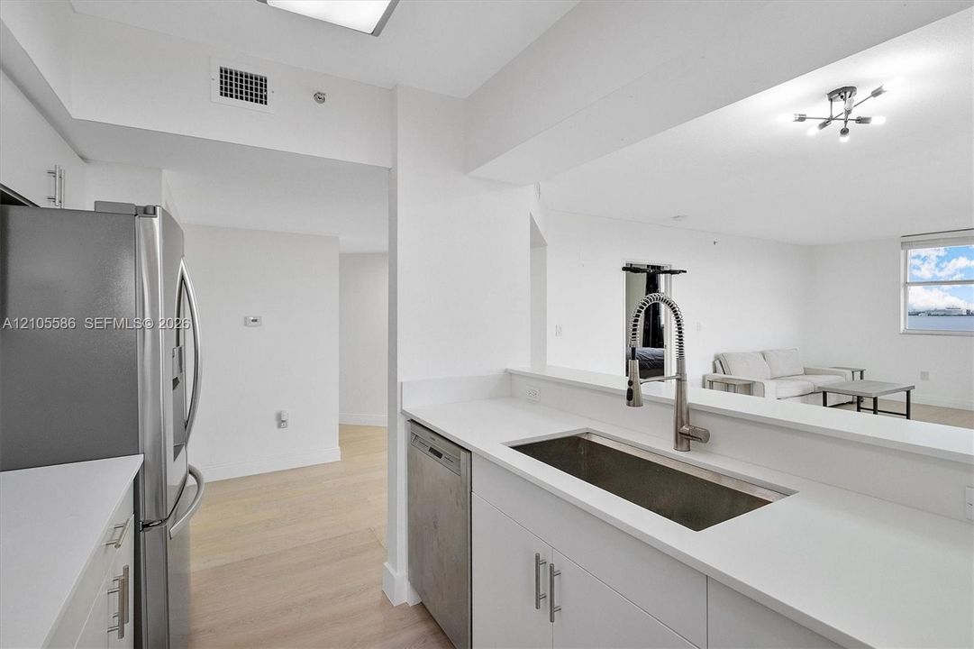 Contemporary kitchen featuring white cabinetry, light countertops, stainless steel appliances, and wood-finish flooring