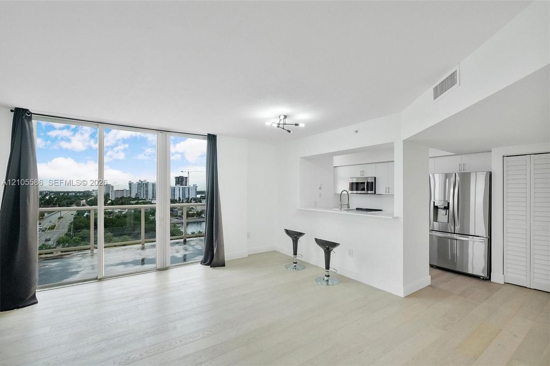 Spacious living area featuring light wood-finish flooring, floor-to-ceiling sliding glass doors, and a contemporary light fixture