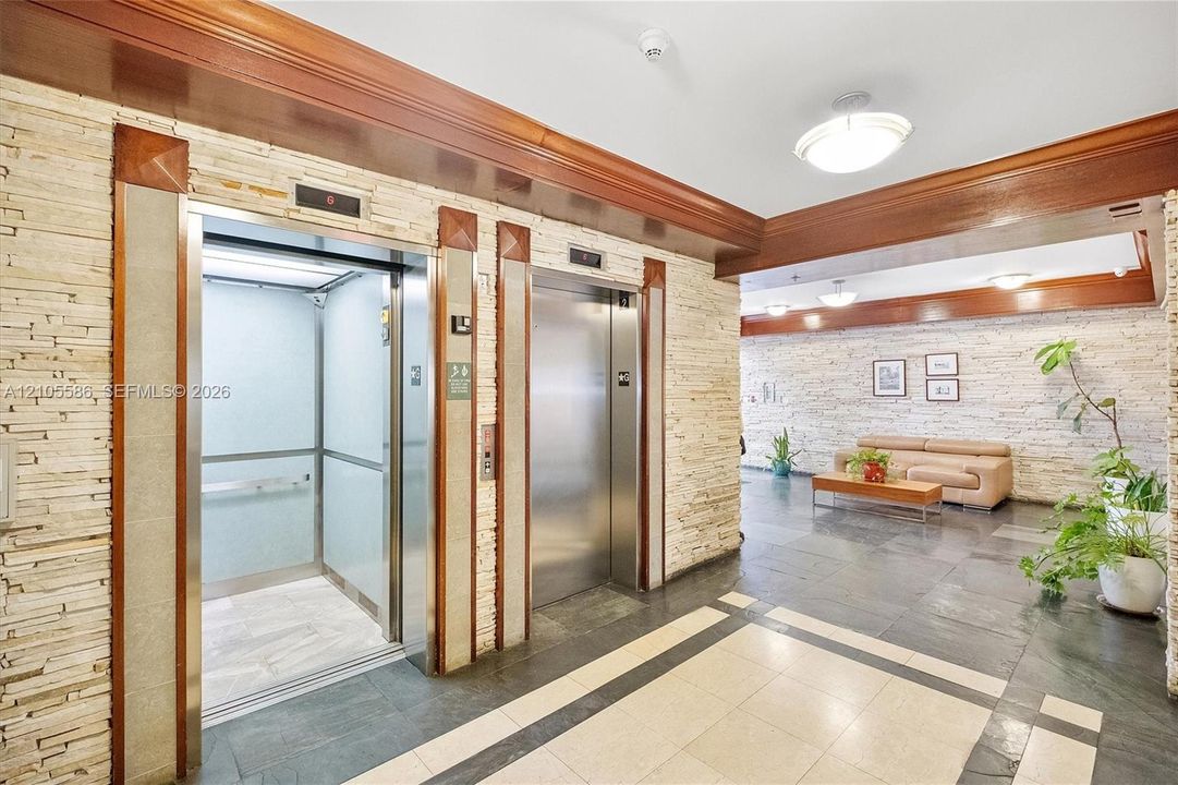 Building lobby featuring dual elevators, stone-finish accent walls, dark stone tile flooring, and wood-finish ceiling trim