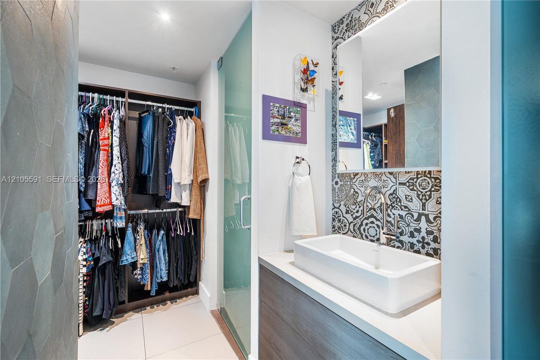Built-in closet system, tile flooring, glass shower enclosure, vanity with basin sink, and patterned wall tile