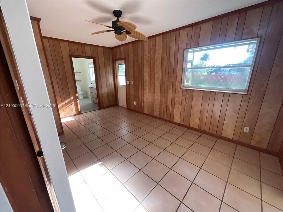 Interior space featuring wood-paneled walls, neutral-toned square tile flooring, a ceiling fan, and a single-hung window