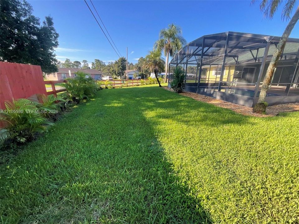 Fenced backyard featuring a manicured lawn, landscaping, and a screened-in pool enclosure