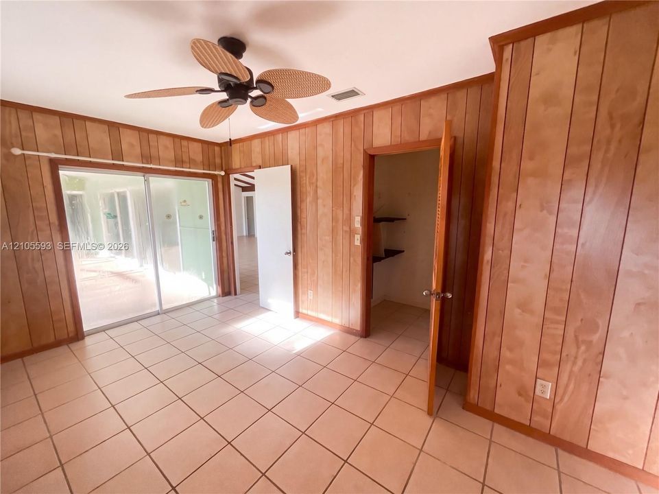 Interior featuring wood-paneled walls, tile flooring, sliding glass doors, and a ceiling fan with integrated lighting