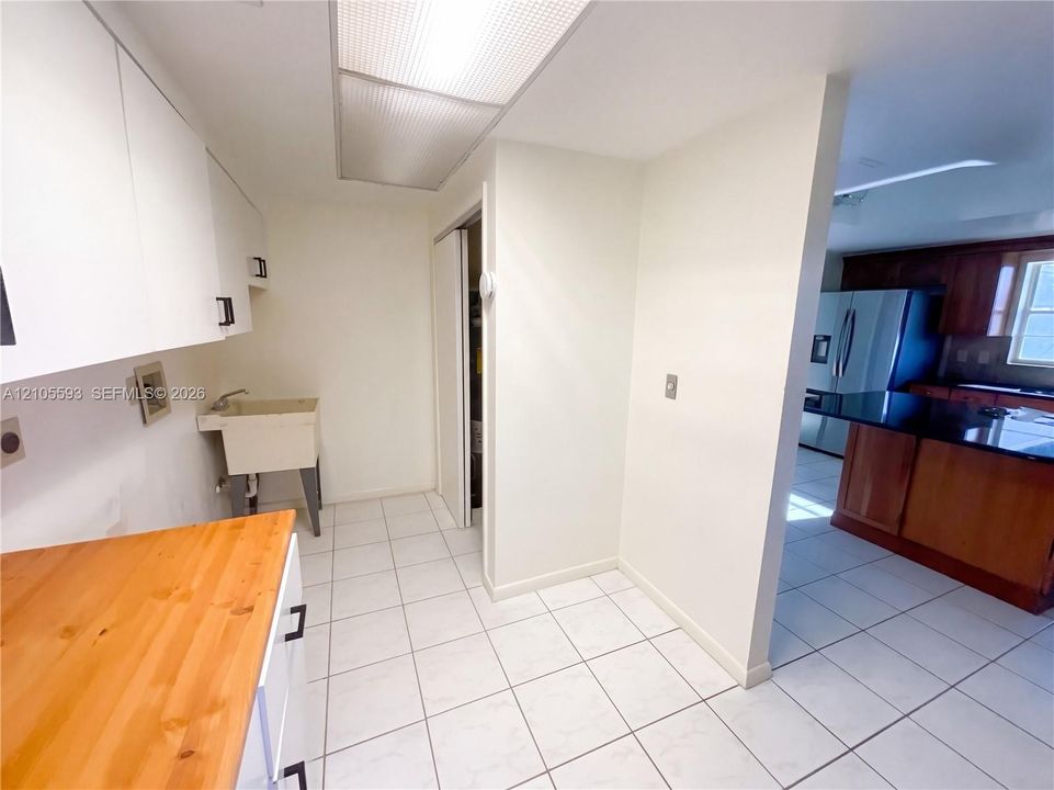 Utility space featuring white cabinetry, a butcher-block countertop, and a wall-mounted utility sink with tiled flooring