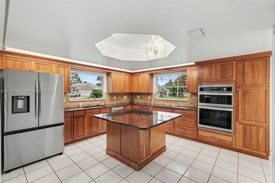 Kitchen featuring custom wood cabinetry, central island with stone countertop, stainless steel double wall oven, stainless steel refrigerator, and vaulted octagonal ceiling