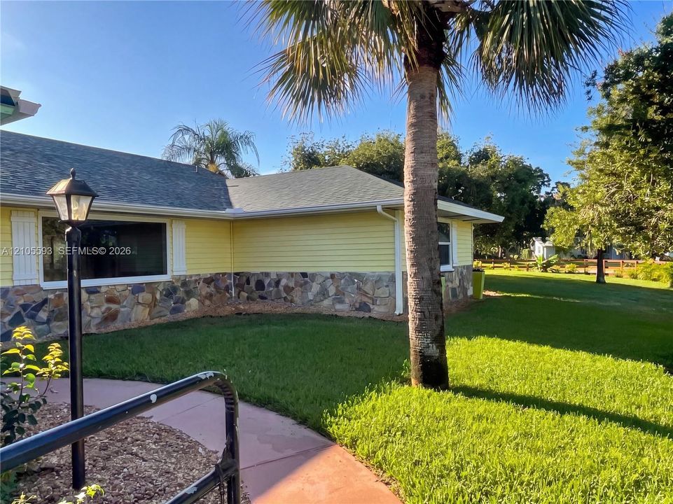 Exterior featuring light-colored horizontal siding, natural stone wainscoting, a shingled roof, a curved concrete walkway, and a mature palm tree