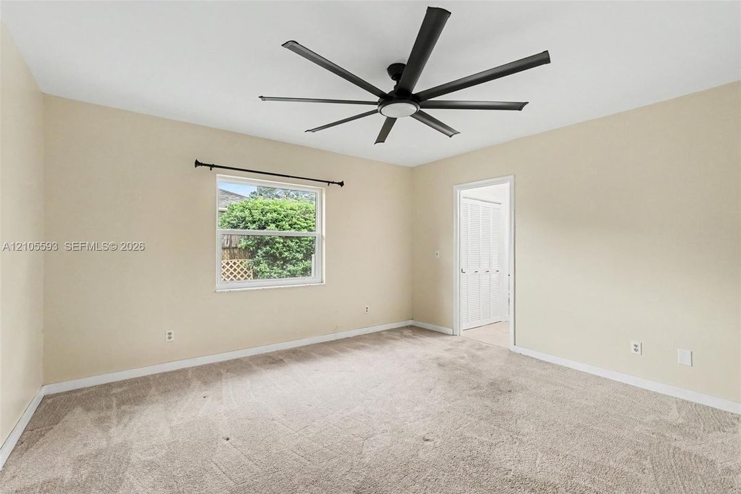 Neutral-toned room featuring wall-to-wall carpeting, a multi-blade ceiling fan, and a window with a metal rod