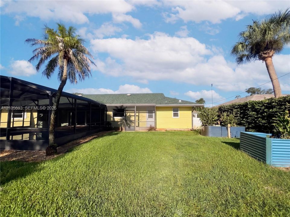 Backyard featuring a screened-in lanai, yellow horizontal siding, a green shingle roof, and corrugated metal garden beds