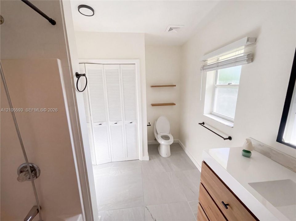 Bathroom featuring a vanity with a white countertop, wood-finish cabinetry, matte black hardware, large-format tile flooring, and a bifold closet