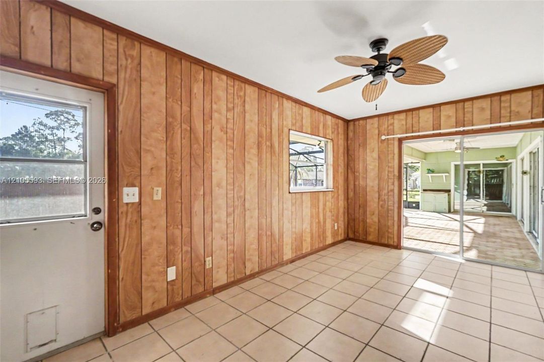Room featuring wood-panel wall finishes, tile flooring, a multi-blade ceiling fan, a window with exterior exposure, and sliding glass doors