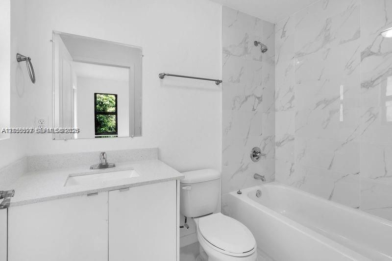 Bathroom featuring a stone-finish countertop, white cabinetry, a rectangular sink with a chrome faucet, and a shower-tub combination with large-format wall tile