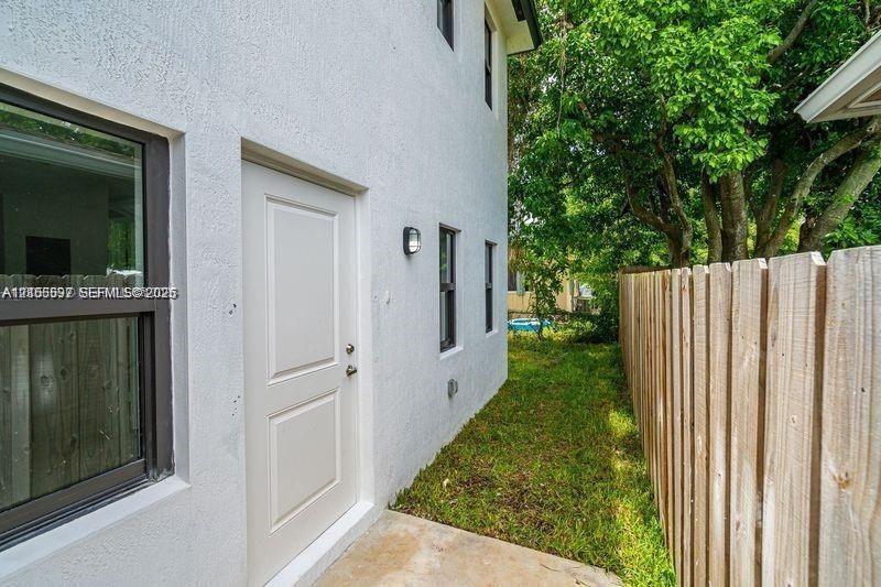 Stucco exterior finish with a dedicated side entry door, aluminum-frame windows, exterior wall-mounted lighting, and a wood privacy fence