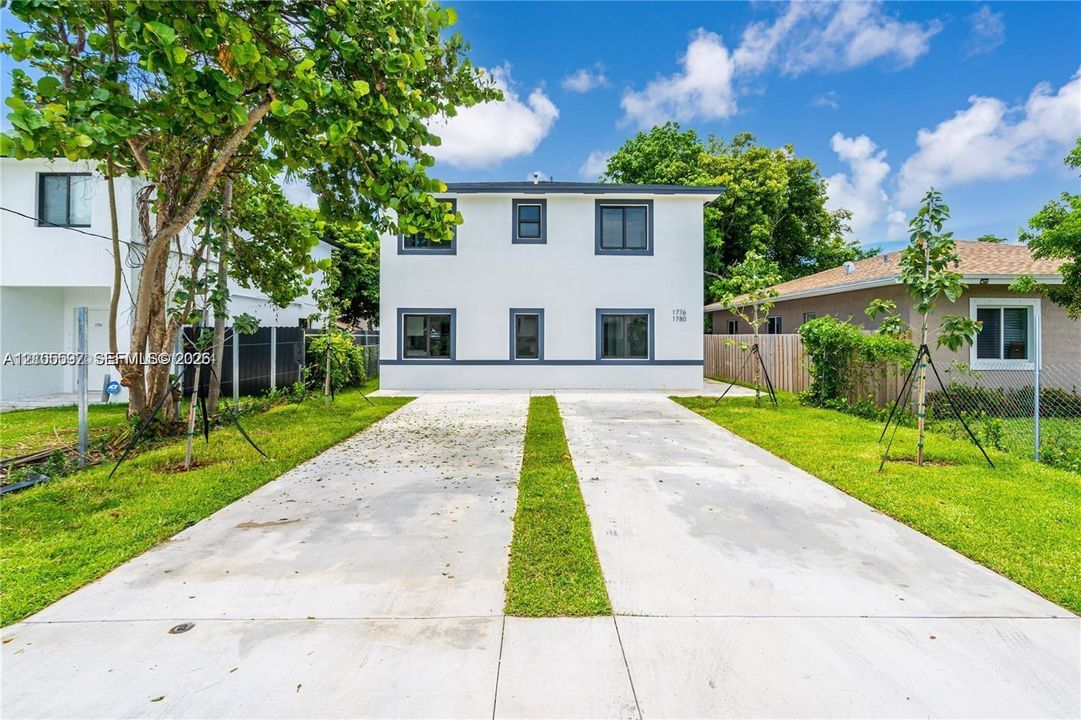 Two-story exterior featuring a smooth stucco finish, multi-pane windows with dark trim, and a concrete driveway with a central grass inlay