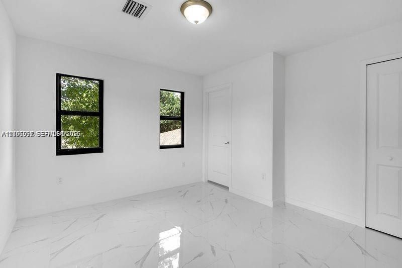 Interior room featuring polished white stone-finish tile flooring, matte black window frames, and two-panel interior doors