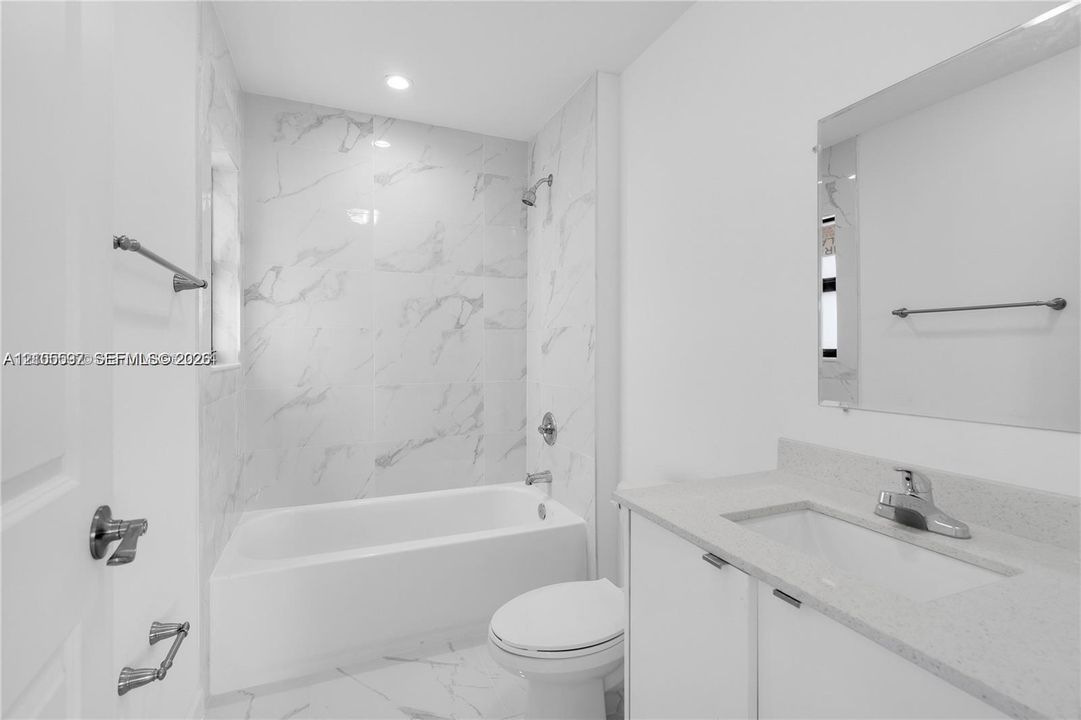 Full-height stone-finish shower surround, porcelain tile flooring, built-in vanity with integrated countertop and sink, and wall-mounted mirror