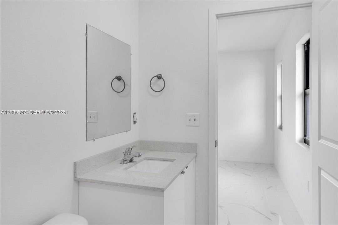 Vanity featuring a stone-surface countertop, rectangular undermount sink, chrome faucet, wall-mounted mirror, and circular towel ring
