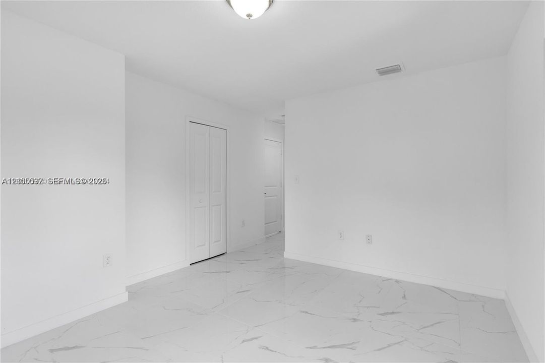 Interior space featuring polished stone-finish tile flooring, white walls, flush-mount ceiling lighting, and a closet with bifold doors