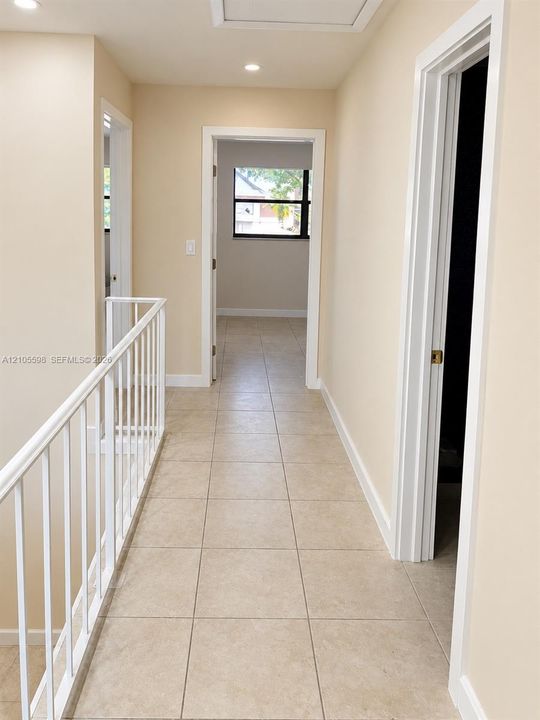Hallway with neutral tone walls, recessed lighting, and square tile flooring