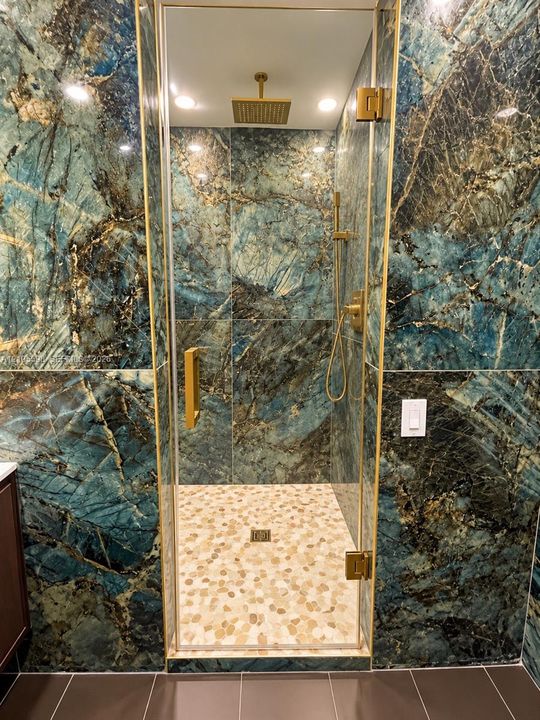 Walk-in shower featuring distinctively veined wall tile, a rain shower head, and gold-finish fixtures
