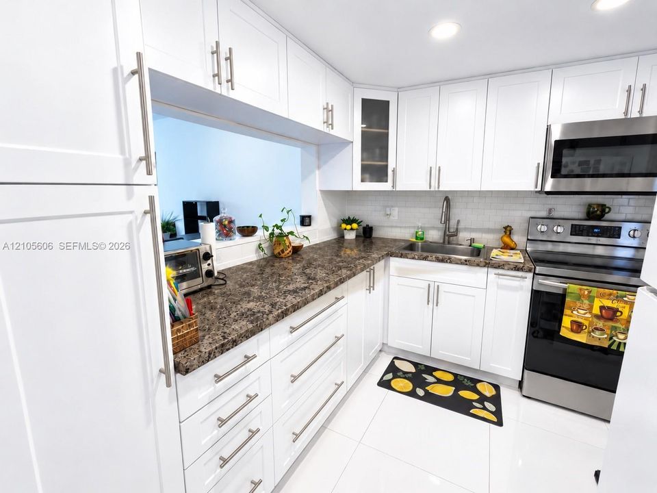White shaker-style cabinetry with brushed nickel hardware, speckled countertops, stainless steel appliances, and white tile flooring