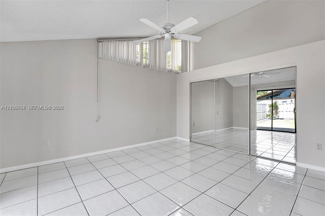 Vaulted ceiling with a ceiling fan, white tile flooring, and mirrored closet doors