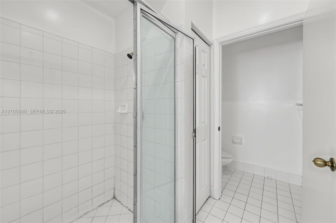 Shower stall with a glass door, white wall tiling, and white floor tiling