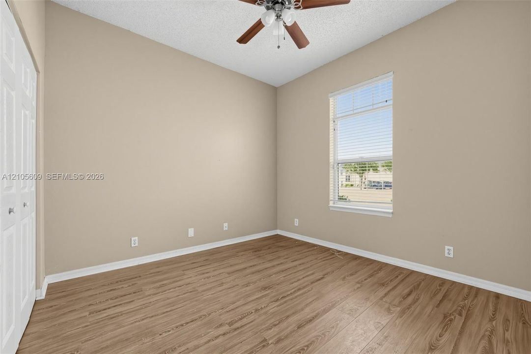Room featuring wood-finish flooring, a ceiling fan with integrated lighting, textured ceiling, and double-door closet cabinetry