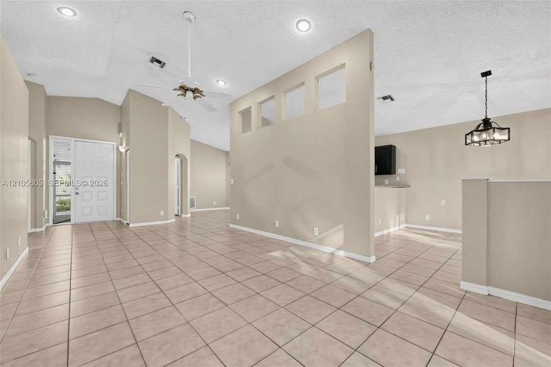 Ceramic tile flooring, vaulted ceilings with recessed lighting, interior partition wall with cutout architectural niches, and a multi-light pendant fixture