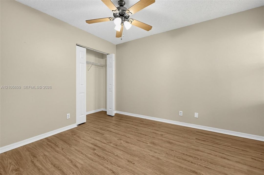 Room featuring wood-finish flooring, neutral wall paint, a ceiling fan with integrated lighting, and a closet with bifold doors