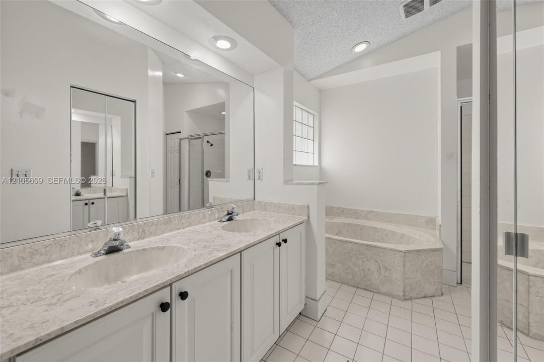 Dual-sink vanity with stone-finish countertop, full-width mirror, recessed lighting, and separate built-in soaking tub with surround