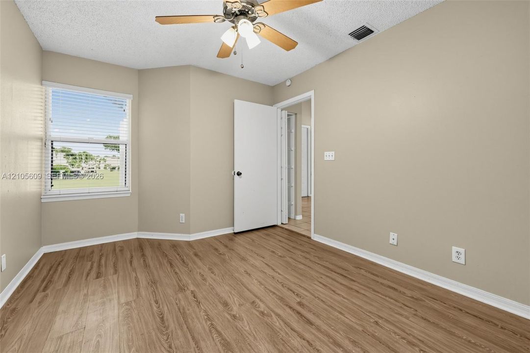 Neutral-toned interior space featuring wood-finish flooring, a multi-pane window, and a ceiling-mounted light fixture with a central fan