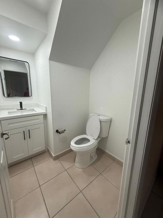 White vanity cabinet with a stone-surface countertop, rectangular integrated sink, matte black faucet, ceramic floor tiling, and a black-framed mirror