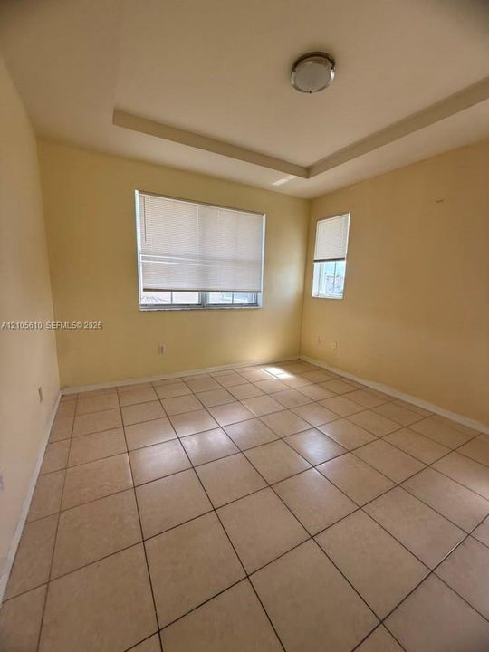 Room featuring a tray ceiling, neutral-toned tile flooring, and dual windows with fitted blinds
