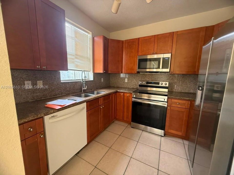 Kitchen featuring stained-wood cabinetry, stone-finish countertops, stainless steel appliances, a dual-basin sink, and ceramic tile flooring