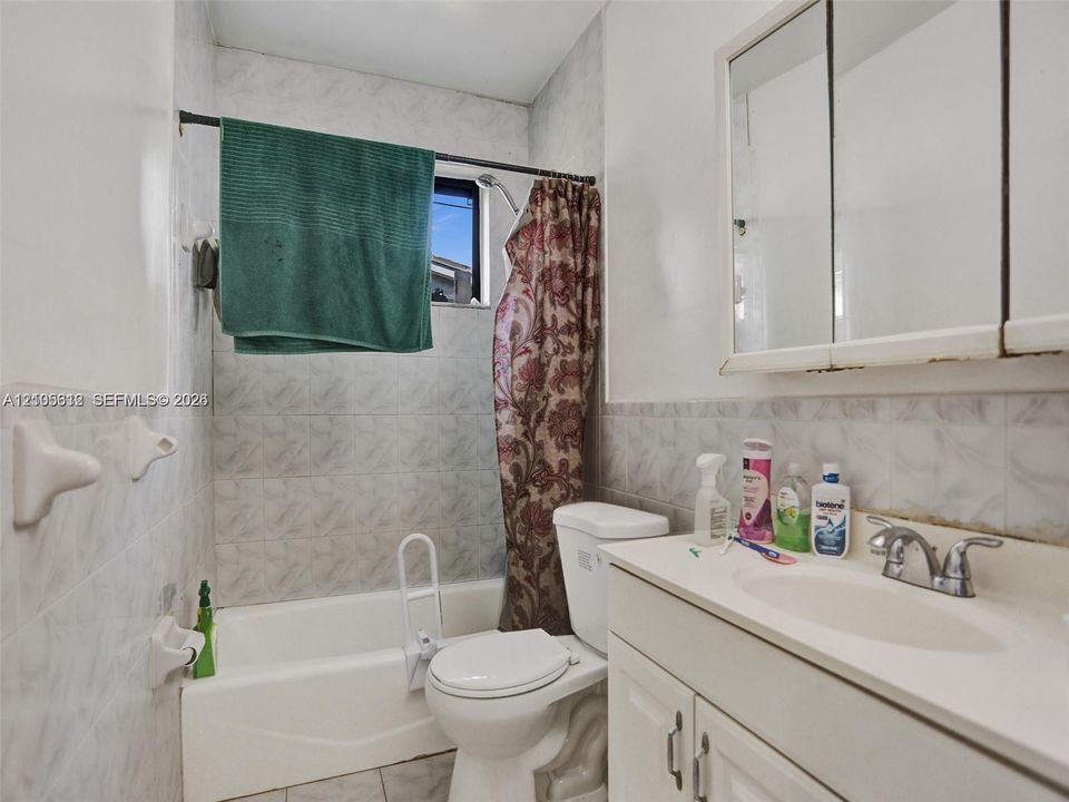 Bathroom featuring a porcelain tub and shower combination, wall-mounted medicine cabinet with mirrors, vanity with an integrated sink, and light-toned tile wall surfacing