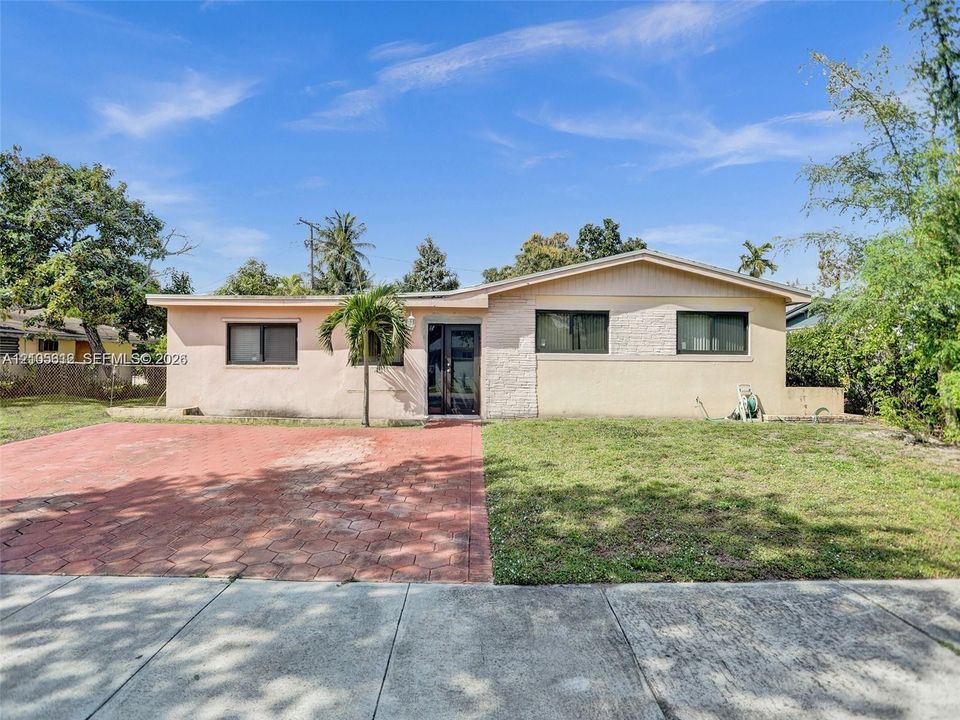 Single-story residence featuring a painted masonry exterior with textured stone facade detailing, a low-pitch roofline, and a paved hexagonal-patterned driveway