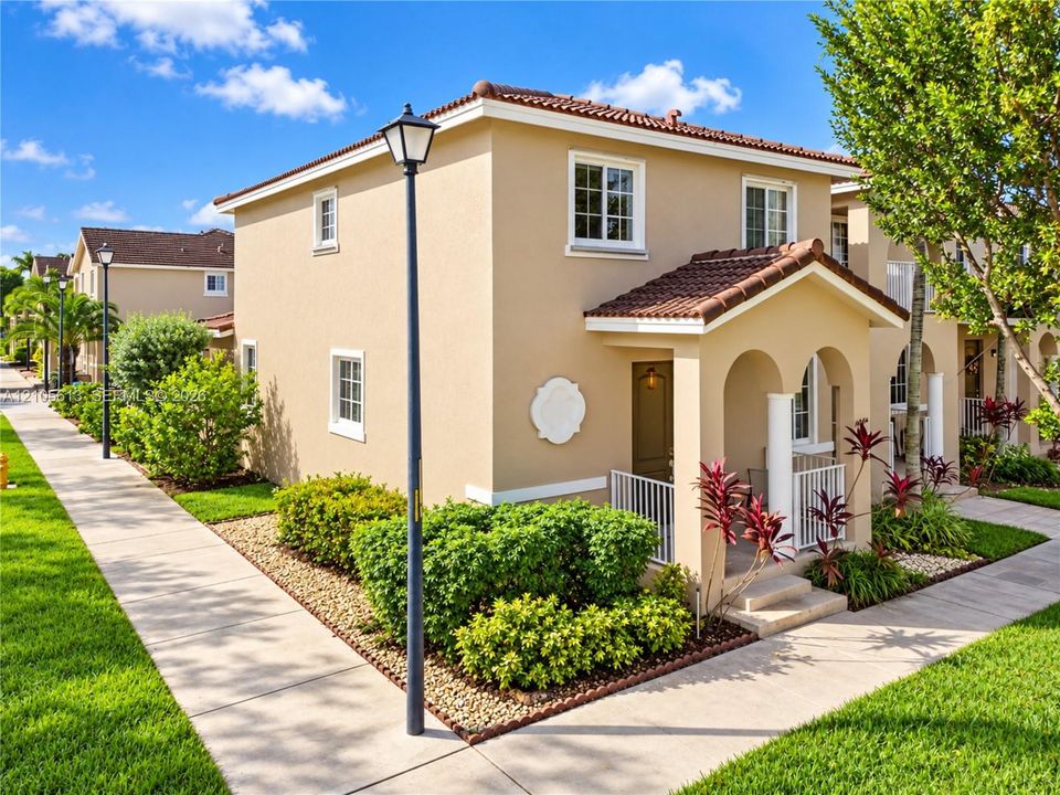 Stucco exterior featuring a covered entryway with arched openings, tiled roof, white-trimmed windows, and decorative architectural medallion