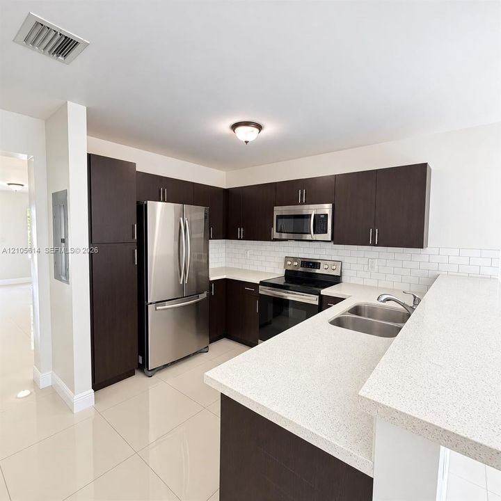 Kitchen featuring dark wood-finish cabinetry, light-toned composite countertops, a subway tile backsplash, stainless steel appliances, and tile flooring