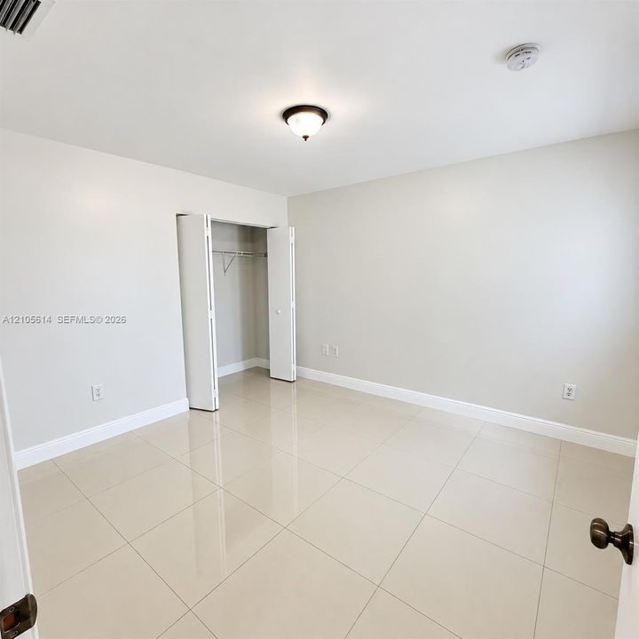 Neutral-toned room featuring large-format tile flooring, a walk-in closet with double-hinged doors, and a central ceiling-mounted light fixture