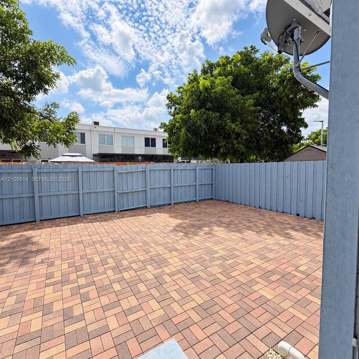 Private courtyard featuring herringbone-patterned paver flooring and full-perimeter wood fencing