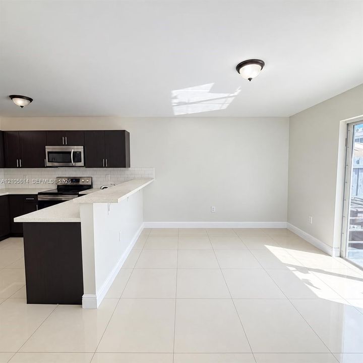 Kitchen featuring dark-finish cabinetry, stone-composite countertops, breakfast bar, white tile backsplash, and ceramic floor tiling