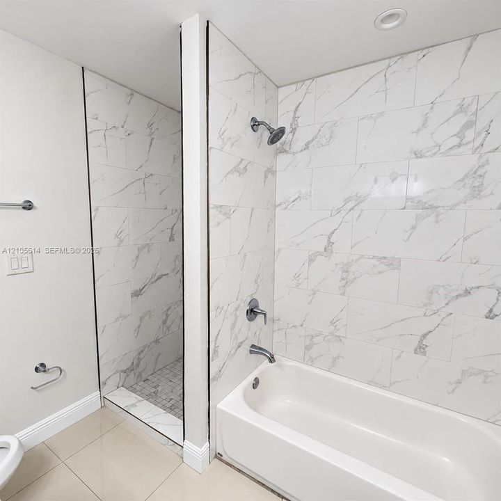 Shower and bathtub combination featuring large-format white stone-finish tile surround with gray veining, chrome plumbing fixtures, and a recessed tiled shower floor