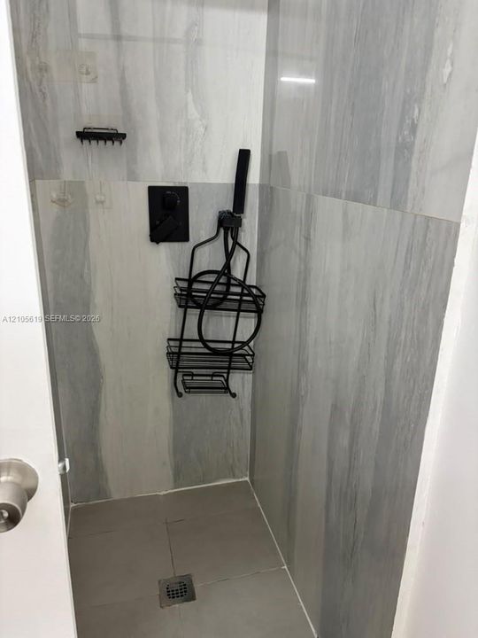 Walk-in shower featuring large-format gray veined tile, matte black wall-mounted faucet, and square floor drain