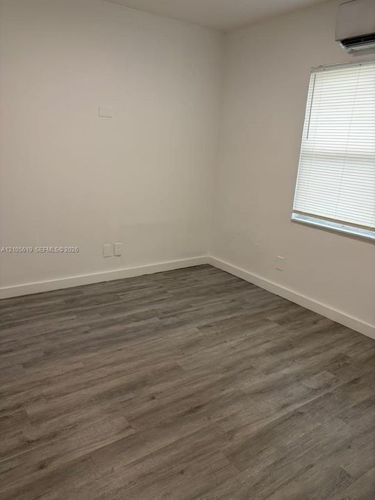 Room featuring wood-finish flooring, neutral wall paint, and a wall-mounted ductless climate control unit