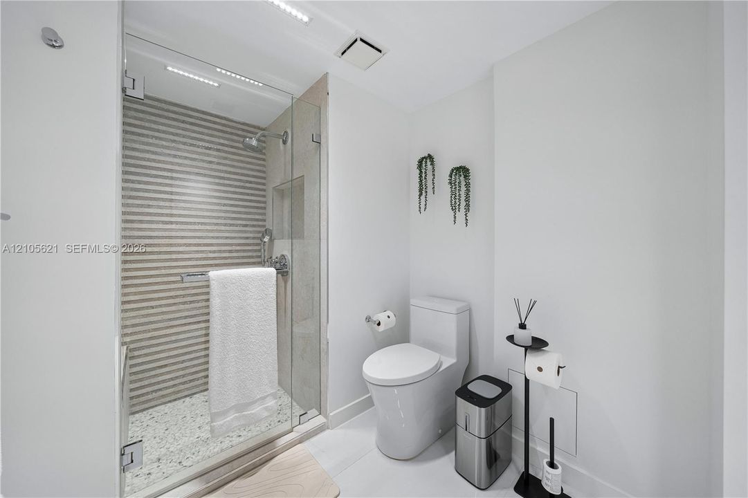 Glass-enclosed shower featuring a textured tile accent wall, built-in recessed wall niche, and stone-finish shower floor