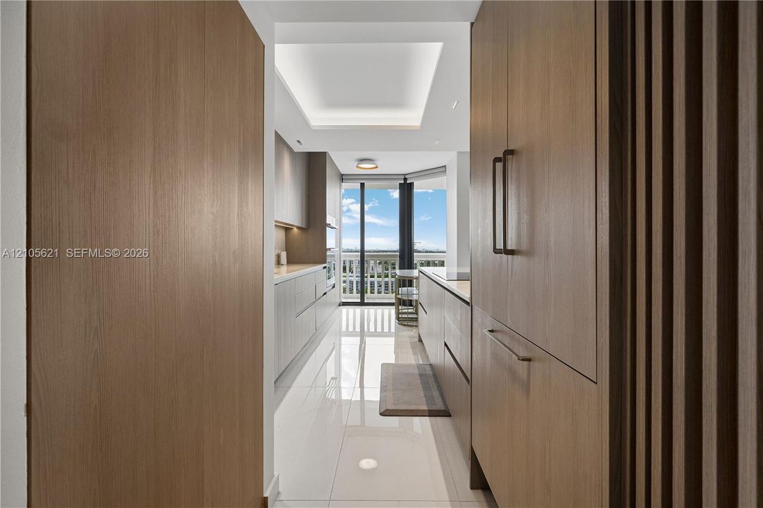 Kitchen featuring custom wood-finish cabinetry, floor-to-ceiling paneling, neutral stone countertops, polished tile flooring, and a recessed tray ceiling