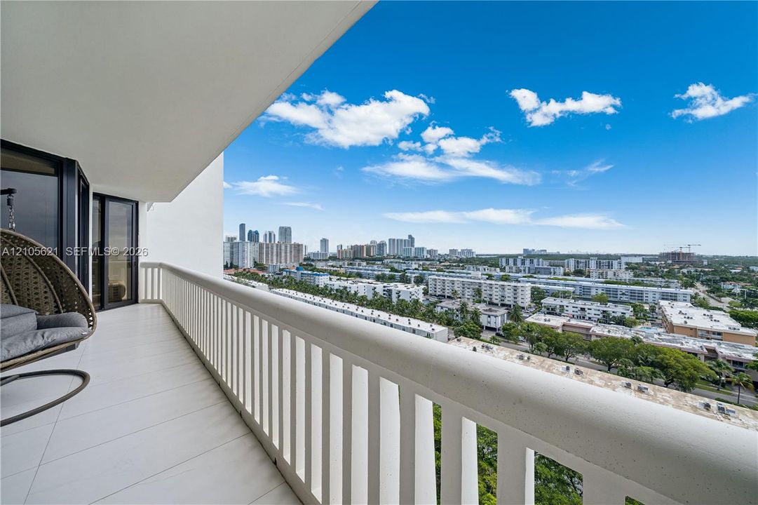 Covered balcony with large-format tile flooring and white metal railing, showcasing an expansive cityscape