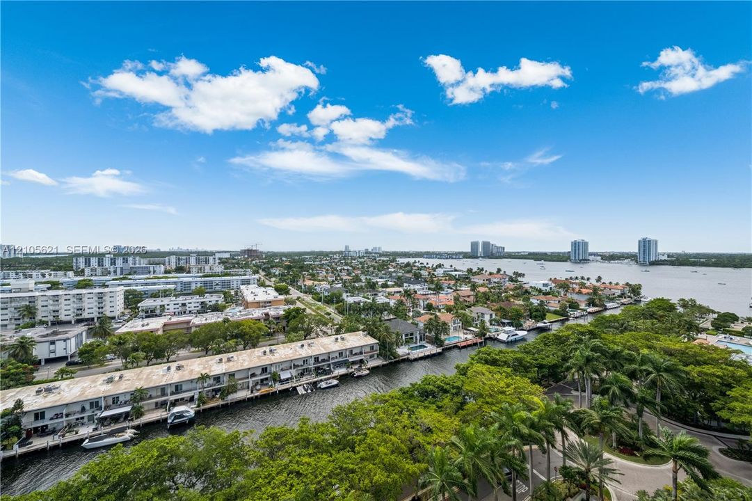 Aerial perspective of coastal landscape featuring deep-water canals, mature palms, residential structures, and direct exposure to a large body of water