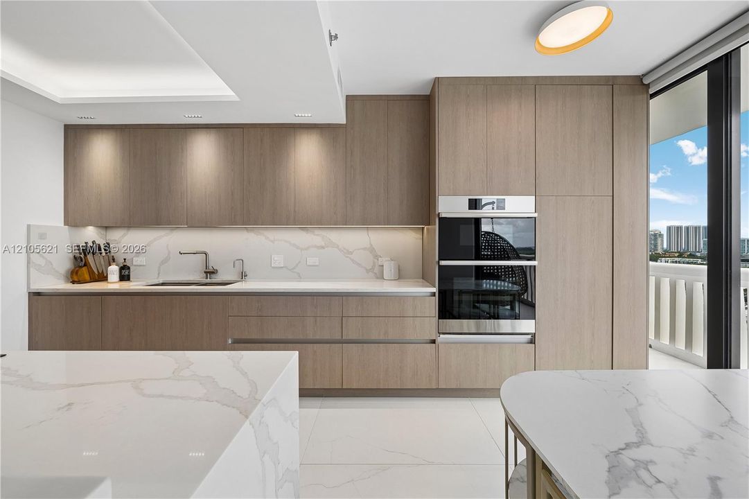 Kitchen featuring flat-panel wood-finish cabinetry, waterfall-edge stone island, integrated stainless steel double oven, and stone slab backsplash