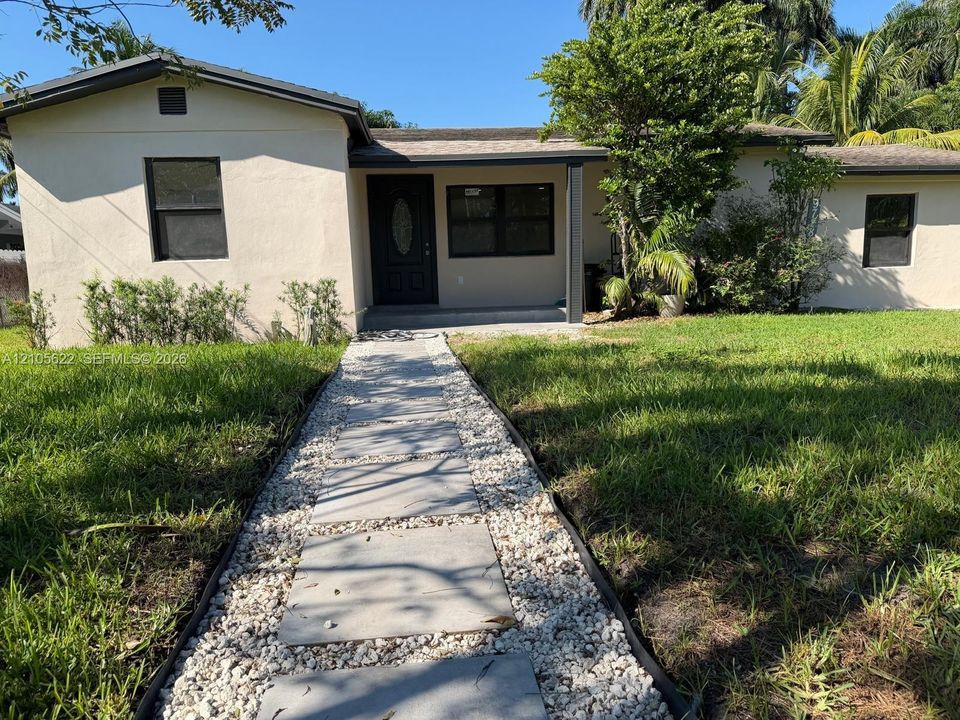 Stucco exterior residence featuring a paved stone walkway with decorative gravel borders, an oval-paneled front entry door, and a covered porch area